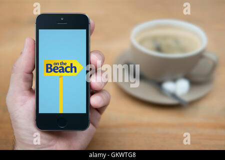 Ein Mann schaut auf seinem iPhone die On The Beach-Logo anzeigt, während bei einer Tasse Kaffee (nur zur redaktionellen Verwendung) saß. Stockfoto