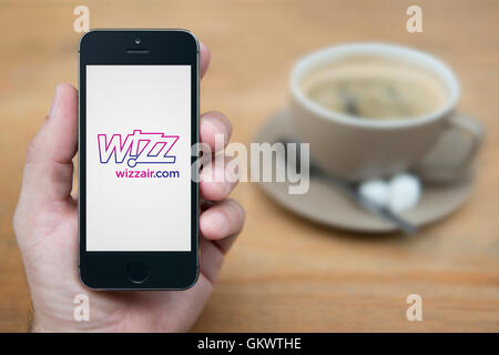 Ein Mann schaut auf seinem iPhone die Wizz-Logo anzeigt, während bei einer Tasse Kaffee (nur zur redaktionellen Verwendung) saß. Stockfoto