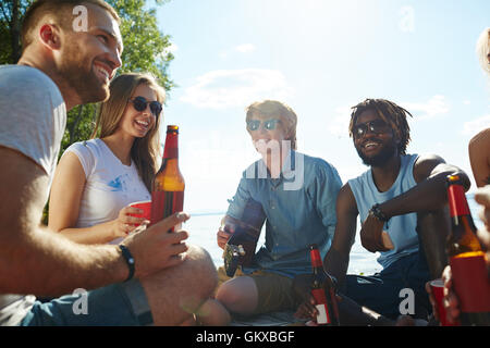 Gruppe von jungen Leuten am Strand sitzen und Bier trinken Stockfoto
