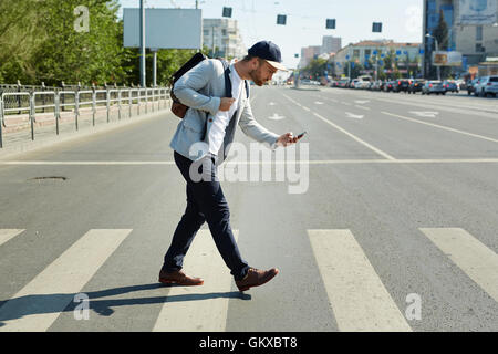 Junger Mann mit Handy-spielen augmented-Reality-Spiel während der Überfahrt Straße Stockfoto