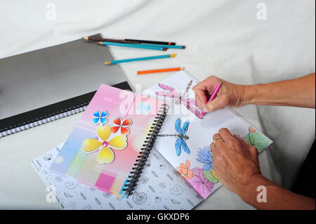 Die Hände der erwachsenen Frau. Malvorlagen in Malbuch. Stifte und Notizbücher auf Tisch herumliegen. Stockfoto