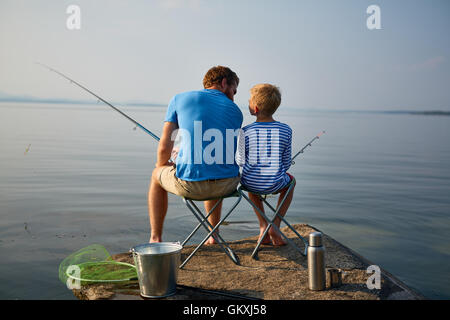 Junge und sein Vater mit Stangen sitzen auf Stühlen von See Stockfoto