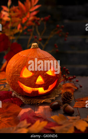 Brennen von Jack O'Lantern auf einem rustikalen Tisch mit herbstlichen Dekorationen, beleuchtet dunkel. Stockfoto