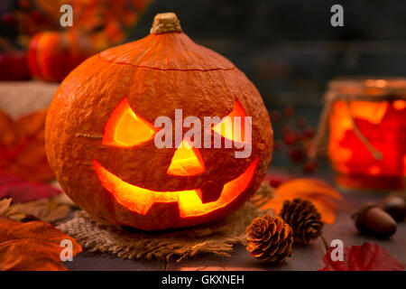 Brennen von Jack O'Lantern auf einem rustikalen Tisch mit herbstlichen Dekorationen, beleuchtet dunkel. Stockfoto