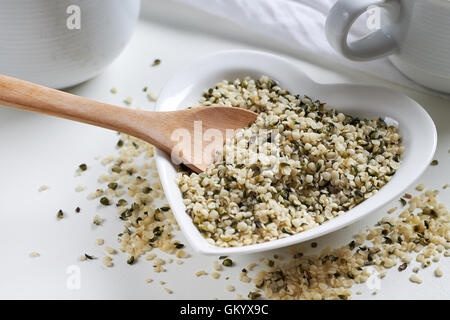 Hanfsamen in Herzen geformt, Keramikschale und Kochlöffel auf weißem Hintergrund Stockfoto