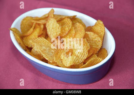 Frisch gebratene Kartoffelchips in einer blauen Schüssel auf einem rosa Tisch Stockfoto