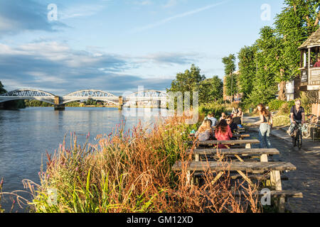 Eine Gruppe junger Menschen, die an einem Sommerabend in Barnes, London, SW13, England, einen Drink und eine entspannte Atmosphäre an der Themse genießen Stockfoto