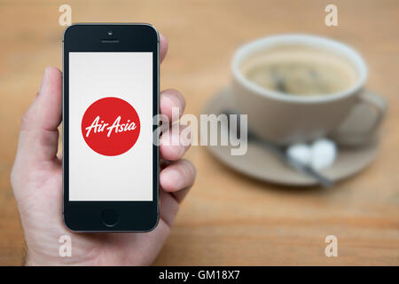 Ein Mann schaut auf seinem iPhone die Air Asia-Logo anzeigt, während bei einer Tasse Kaffee (nur zur redaktionellen Verwendung) saß. Stockfoto