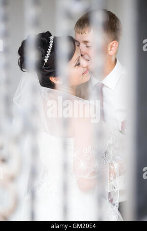 Junge kaukasischen Brautpaar küssen im Freien. Schöne glückliche Braut, kuscheln und küssen mit schönen Bräutigam bei der Hochzeit Stockfoto