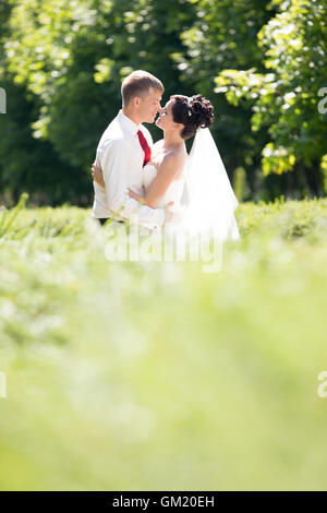 Junge kaukasischen Brautpaar küssen im Freien. Wunderschöne Brautpaar umarmen und küssen am Tag der Hochzeit im Sommer. Liebe Stockfoto