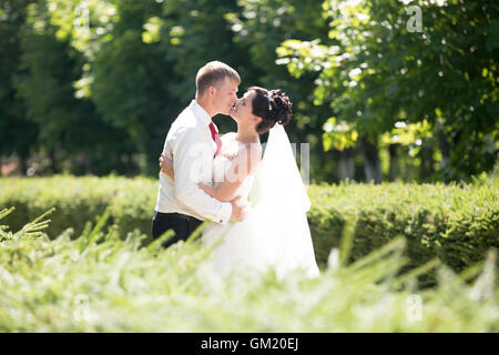 Junge kaukasischen Brautpaar küssen im Freien. Wunderschöne Brautpaar am Tag der Hochzeit im Sommer zu küssen. Liebe und glücklich Stockfoto