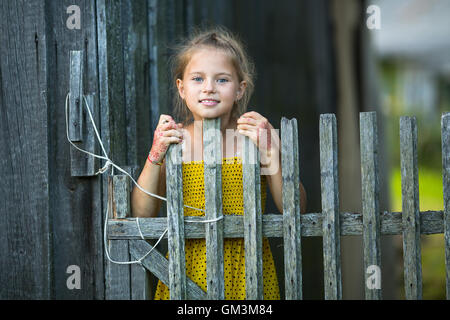 Porträt der niedliche kleine Mädchen in der Nähe der Holzzaun im Dorf. Stockfoto