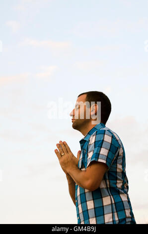 Mann stehend und auf einem Hügel außerhalb mit seine Hände zusammen beten. Stockfoto