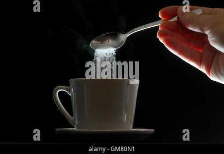 Hand strömenden Braunzucker in weißen Tasse Kaffee Stockfoto