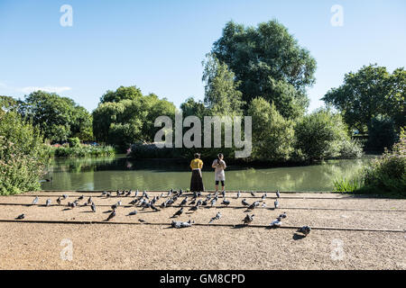 Zwei junge Frauen, die Fütterung der Ente am Teich Barnes, London, SW13, UK Stockfoto