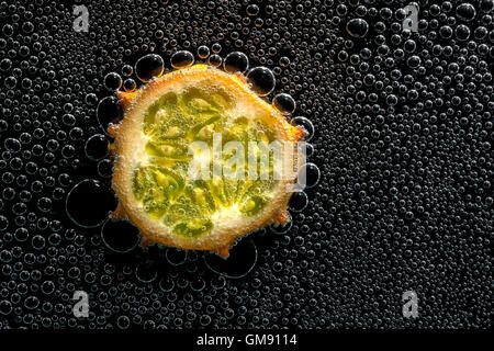 Kiwano, gehörnte Melone Frucht in Mineralwasser, eine Reihe von Fotos. Close-up kohlensäurehaltiges Wasser vor schwarzem Hintergrund Stockfoto