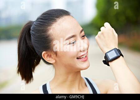 junge Asiatin Läufer zeigen tragbare Fitnessgerät (ansehen) und lächelnd. Stockfoto