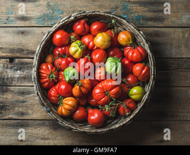 Frische bunte Reifen Urtomaten im Korb über hölzerne Hintergrund Stockfoto