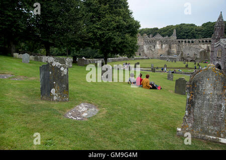 St. Davids Cathedral.Three Freunde sitzen auf dem Rasen umgeben von Grabsteinen mit Blick auf Bischofspalast Stockfoto