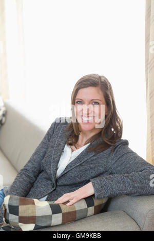 Porträt von lächelnden mittleren Erwachsenenalter Frau sitzend auf sofa Stockfoto