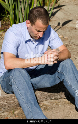 Mann sitzen und beten mit Hände gefaltet und Kopf geneigt. Stockfoto