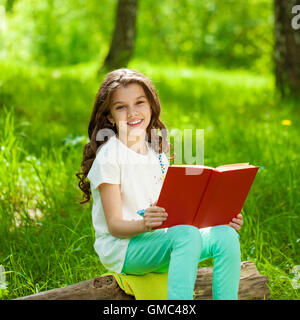 Charmantes kleines Mädchen im Wald mit Buch auf dem Hintergrund der Sommerpark Stockfoto