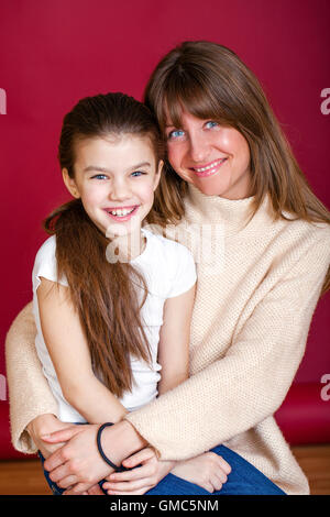 Porträt von sieben Jahre alte Tochter und junge Mutter auf rot isoliert Stockfoto