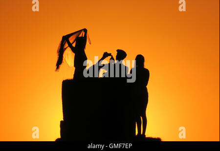 Junge Leute sitzen und stehen auf Heuballen während des Sonnenuntergangs auf Tempelhof Field in Berlin, Deutschland, 25. August 2016. Foto: SOEREN STACHE/dpa Stockfoto