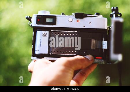 Nahaufnahme der Hand, die die analoge Kamera hält, mit einem Filmstreifen von 35 mm. Rückansicht. Stockfoto