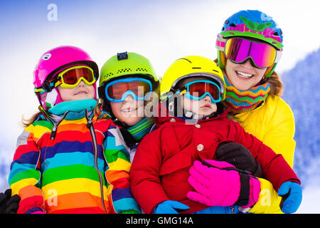 Mutter und Kinder Skifahren in den Bergen. Aktive Mutter und drei Kinder mit Helm, Schutzbrille und Polen. Stockfoto