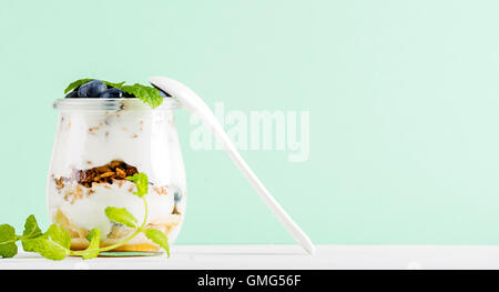 Joghurt-Hafer-Müsli mit Marmelade, Beeren und Blätter in Glas auf Pastell Mint Hintergrund Stockfoto