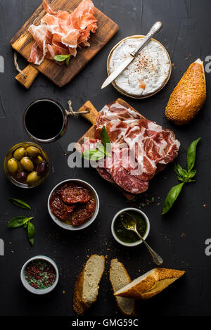 Wein snack Set. Glas Rot, Fleischauswahl, mediterranen Oliven, getrocknete Tomaten, Baguette Scheiben, Camembert Käse und Gewürze auf schwarzem Hintergrund Stockfoto