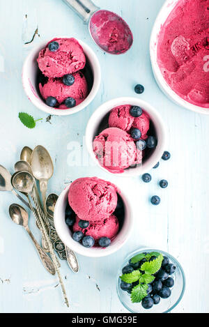 Hausgemachte Heidelbeer-Eis schöpft mit frischen Beeren und Minze in Tassen über hellblauen Hintergrund Stockfoto