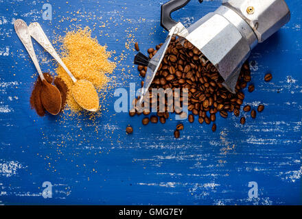 Arabika Eans in Moka Topf, braunem Zucker und Kaffeepulver auf blau lackierten Holztisch Stockfoto