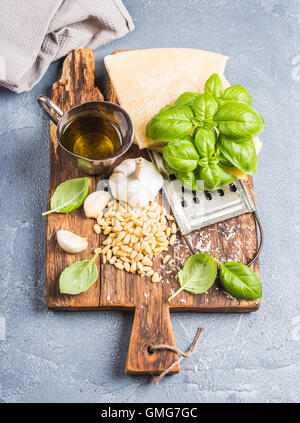 Zutaten für das Pesto-Sauce kochen. Parmesan-Käse, Metall Reibe, frischem Basilikum, Olivenöl, Knoblauch und Pinienkerne auf alten rustikalen Holzbrett über grauen Beton Hintergrund Stockfoto