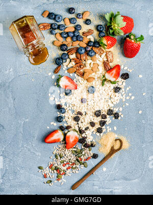 Zutaten für das Kochen gesunden Frühstück.  Erdbeeren, Heidelbeeren, Nüssen, Haferflocken, Trockenobst, Honig mit drizzlier über konkrete strukturiertem Hintergrund Stockfoto