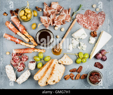 Käse und Fleisch Vorspeise Auswahl oder Wein Snack festgelegt. Vielzahl von Käse, Salami, Schinken, Brot-Sticks, Baguette, Honig, Trauben, Oliven, getrockneten Tomaten, Pecan-Nüssen über grauem Beton texturiert Kulisse, Ansicht von oben. Stockfoto