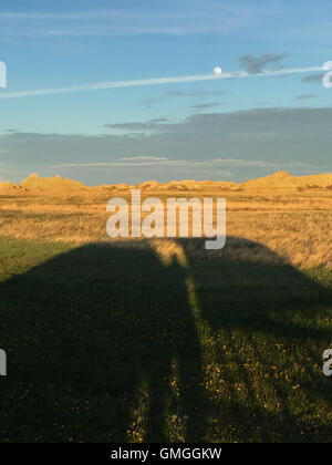 Wenn die Sonne untergeht, erreichen die Schatten eines Zeltes über die Wiesen in Richtung der Badlands mit einem Vollmond über Kopf. Stockfoto