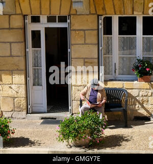 Ein älterer Herr sitzt an seiner Haustür seine Zeitung im September Morgensonne, Dordogne, Frankreich Stockfoto