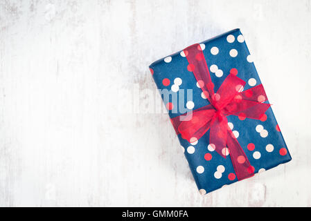 Geschenkbox verpackt in blau gepunktete Papier mit rotem Band auf weißem Holz alte Hintergrund Stockfoto