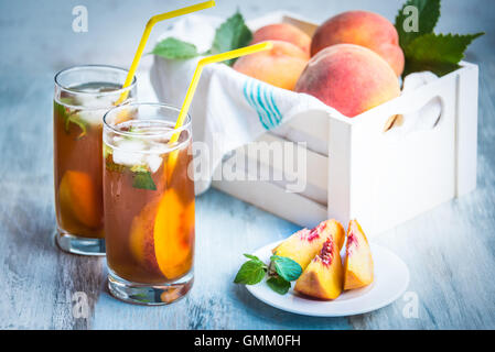 Gläser mit hausgemachten Eistee, Pfirsich gewürzt. Frisch geschnitten Sie Pfirsiche Scheiben für Anordnung. Weiße Kiste voller Pfirsiche in der Ba Stockfoto