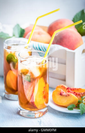 Gläser mit hausgemachten Eistee, Pfirsich gewürzt. Frisch geschnitten Sie Pfirsiche Scheiben für Anordnung. Weiße Kiste voller Pfirsiche in der Ba Stockfoto