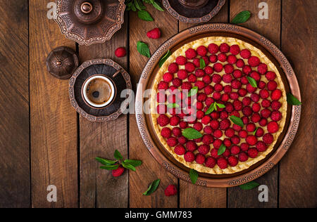 Torte mit Himbeeren und Schlagsahne dekoriert mit Minze auf einem hölzernen Hintergrund. Ansicht von oben Stockfoto