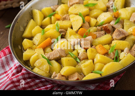 Geschmorte Kartoffeln mit Fleisch in einer Pfanne auf einem Holztisch Stockfoto