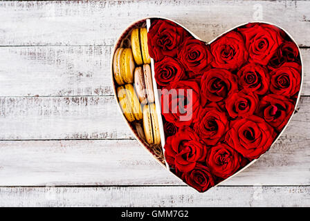 Box in der Form eines Herzens mit roten Rosen und Makronen. Geschenk zum Valentinstag. Ansicht von oben Stockfoto