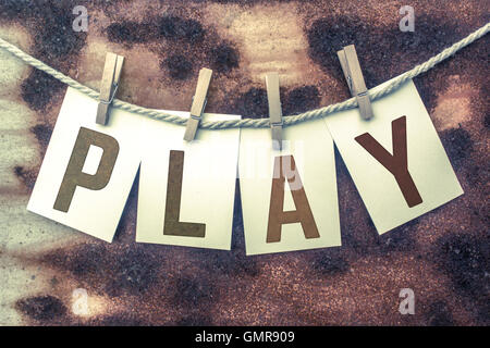 Das Wort "PLAY" auf Karten gestempelt und an einem alten Stück Bindfaden über ein rostiges Metall Hintergrund angeheftet. Stockfoto