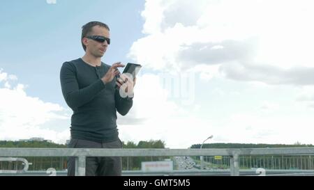 Outdoor Portrait moderner junger Mann mit digital-Tablette. Eine Brille auf der Brücke. Hinter den blauen Himmel Stockfoto
