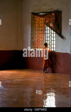 Ein junger Novize sieht aus dem Fenster im Inneren eine Pagode, die Gebäude in einem buddhistischen Tempel in Chork Village, Kambodscha. Stockfoto