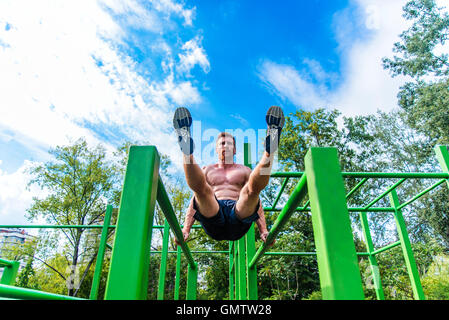 Junger Mann Zug tut ups auf horizontalen Balken im Freien Stockfoto