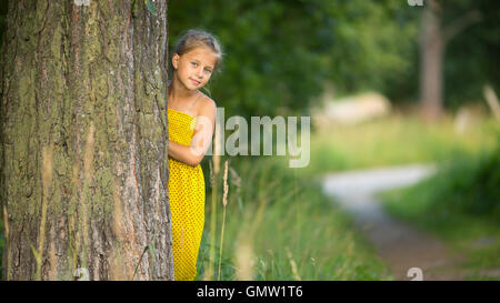 Kleines Mädchen spähen hinter den Baum. Stockfoto